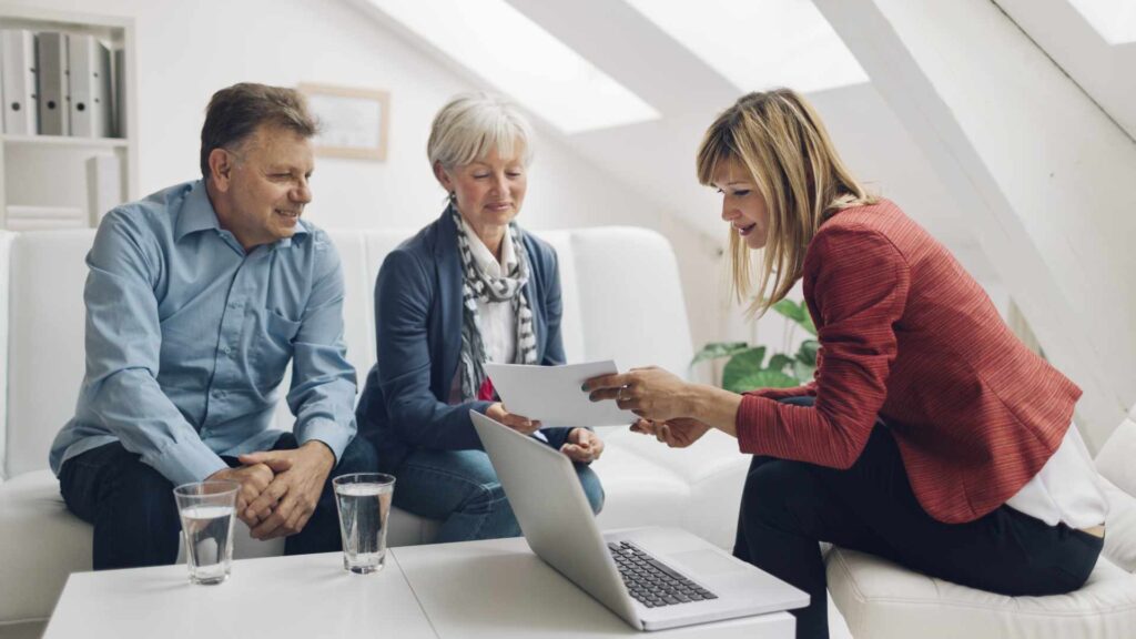 Mature Couple Meeting with Financial Advisor. They are listening to financial advisor. She is speaking about retirement and insurance options for them. Holding contract in her hands and explaining to clients.